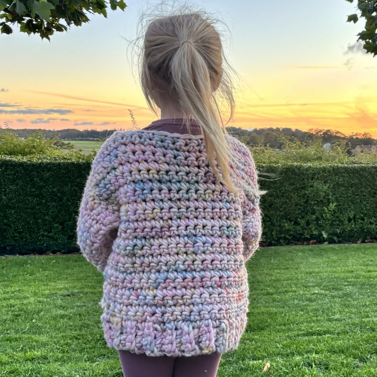 Ryggen af en hæklet børnesweater i pastelfarvet Yarnicorn garn med tydelige fastmasker, lange ærmer og ribkant i taljen.